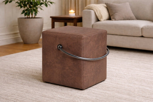 Brauner Polsterhocker in Lederoptik mit Griff im modernen Wohnzimmer, leichter Sitzhocker auf hellem Teppich vor Sofa und Beistelltisch.– Handgefertigte Polsterhocker