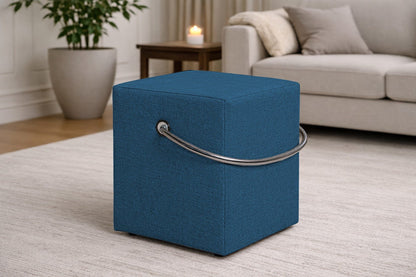 Blauer Polsterhocker mit Griff im modernen Wohnzimmer, leichter Sitzhocker auf hellem Teppich vor Sofa und Beistelltisch.– Handgefertigte Polsterhocker