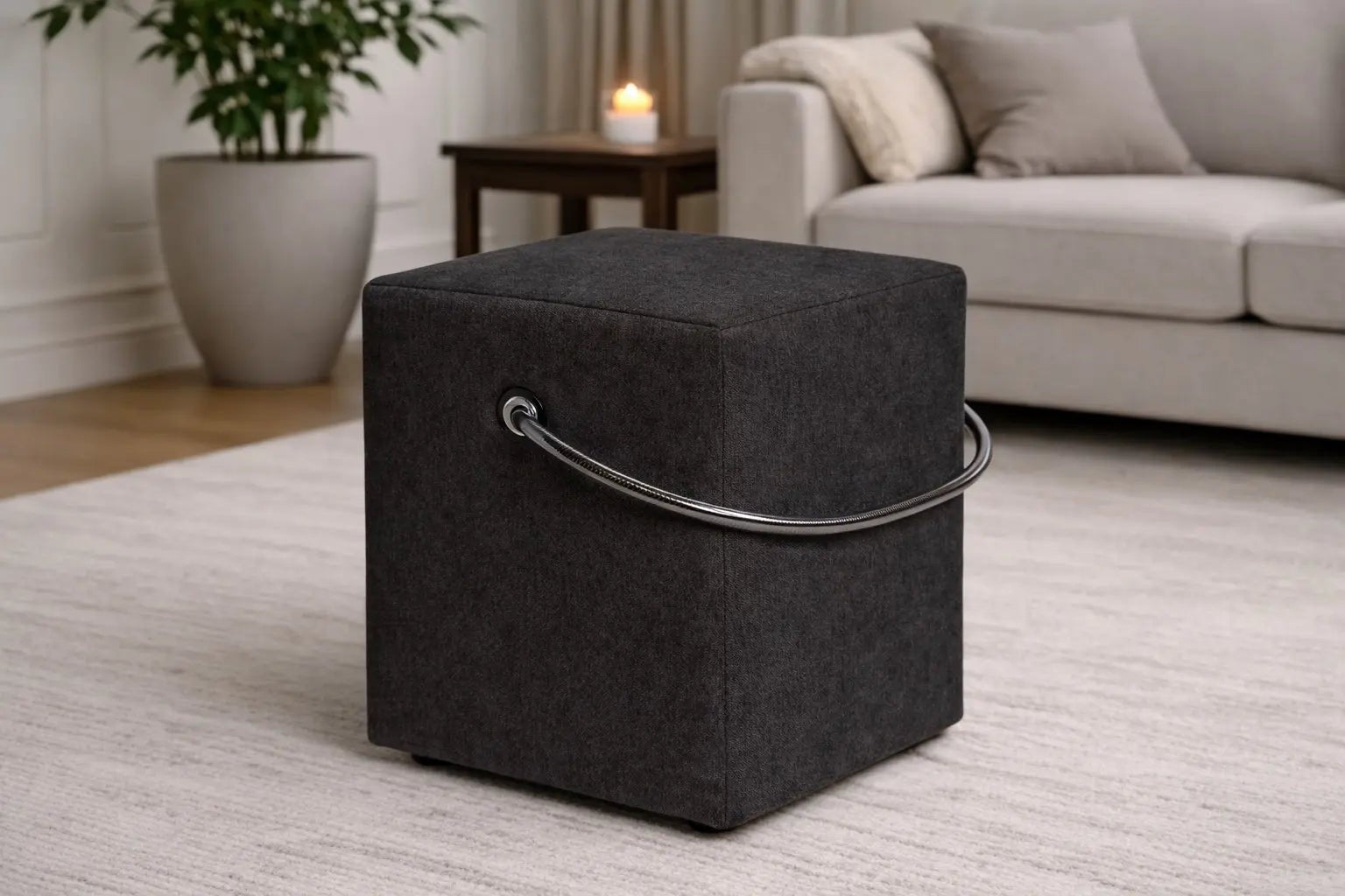 Schwarzer Polsterhocker mit Griff im modernen Wohnzimmer, leichter Sitzhocker auf hellem Teppich vor Sofa und Beistelltisch.– Handgefertigte Polsterhocker